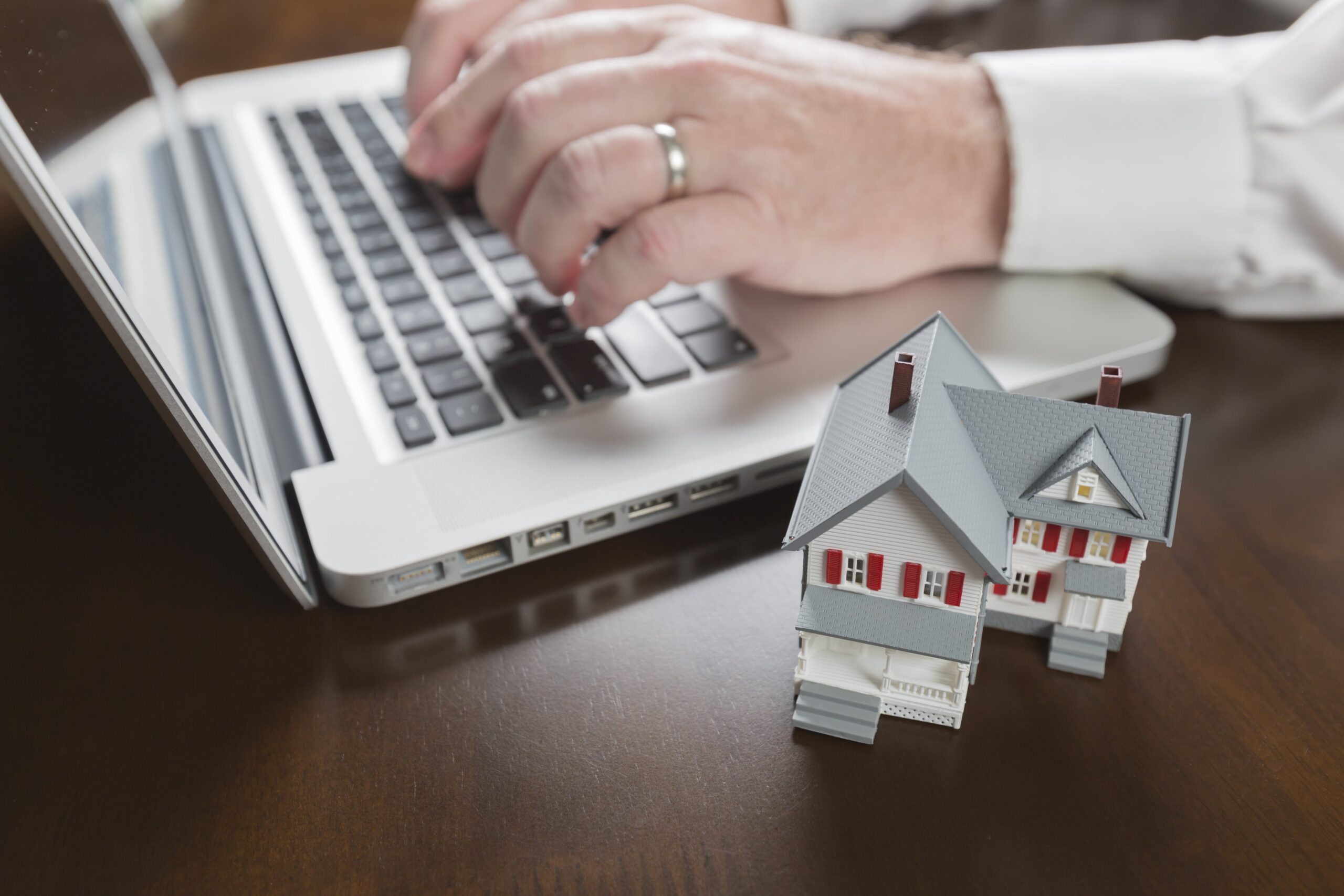 miniature-house-near-man-typing-on-laptop-computer